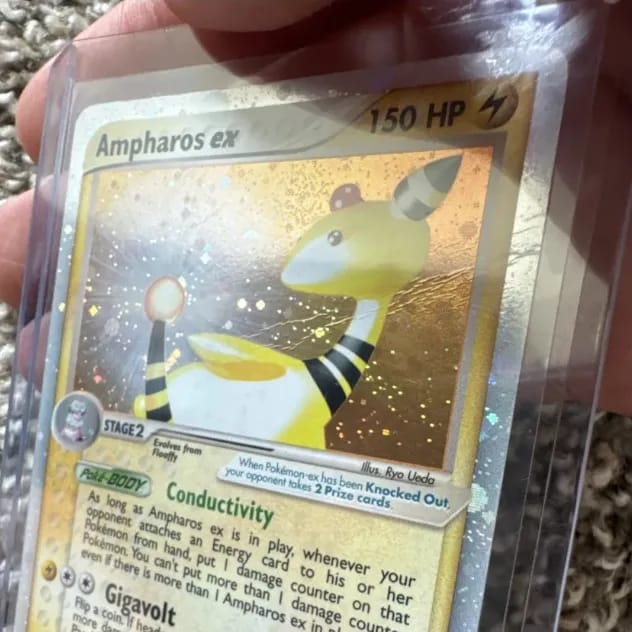 Ampharos ex in a toploader, a wavy crease line catching the light across the holo behind its head.