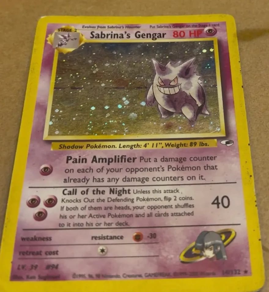 Sabrina’s Gengar lying on a table, dark specks and grime on its yellow border.