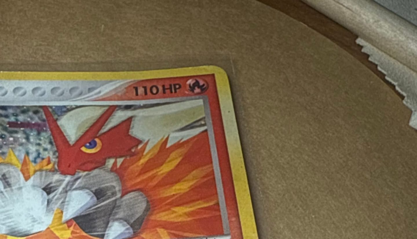 The Blaziken card in a soft sleeve on a brown work mat, a wooden-handled tool and a cloth beside it.