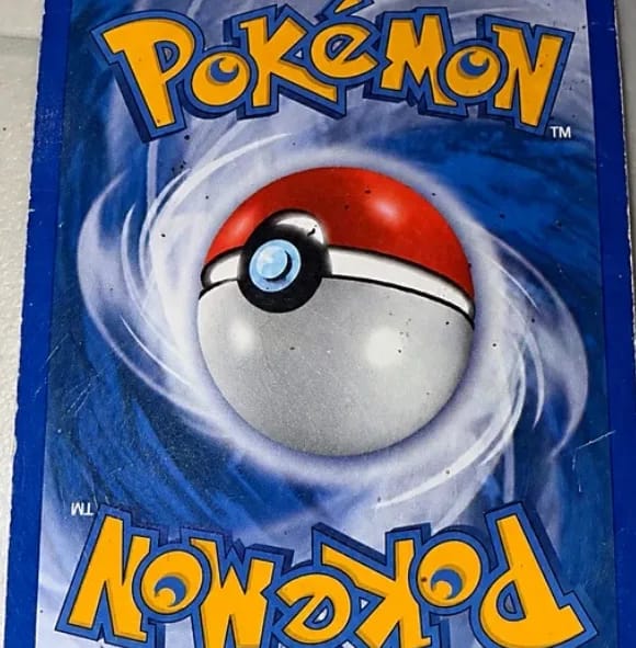 Close-up of the back of a Pokémon card, small dark spots scattered across the blue swirl and the Poké Ball.