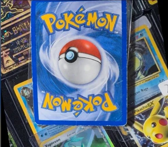 The back of an older Pokémon card lying on a binder of cards, its blue border worn pale at the edges.