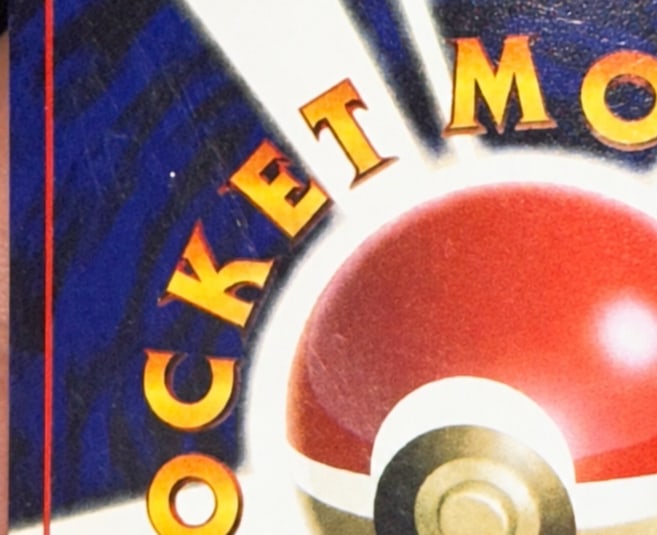 The same part of the same Pocket Monsters card back after the crease was fixed: the blue and the lettering beside the Poké Ball show no crease line, only faint hairline marks.